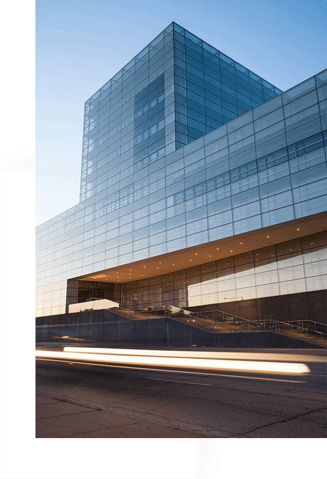 Modern glass building reflecting the sky with light trails from passing vehicles.